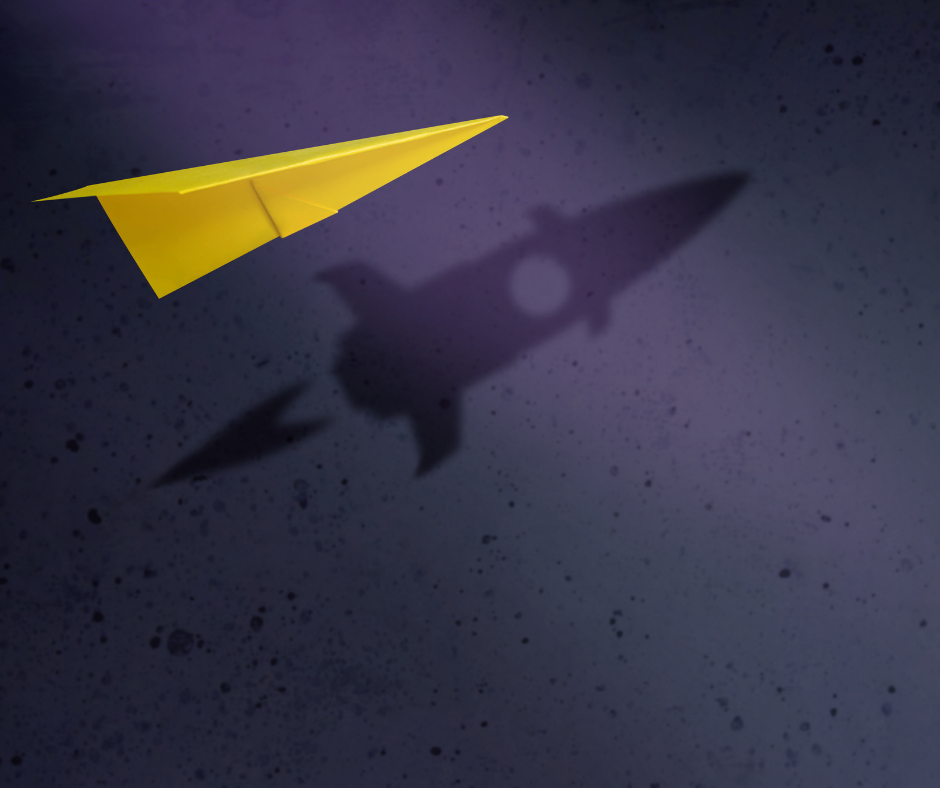 Yellow paper airplane in flight with rocket ship shadow