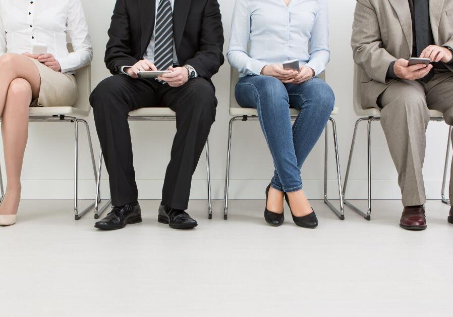 Four people sitting in a row of chairs, waiting with their hands in their laps.