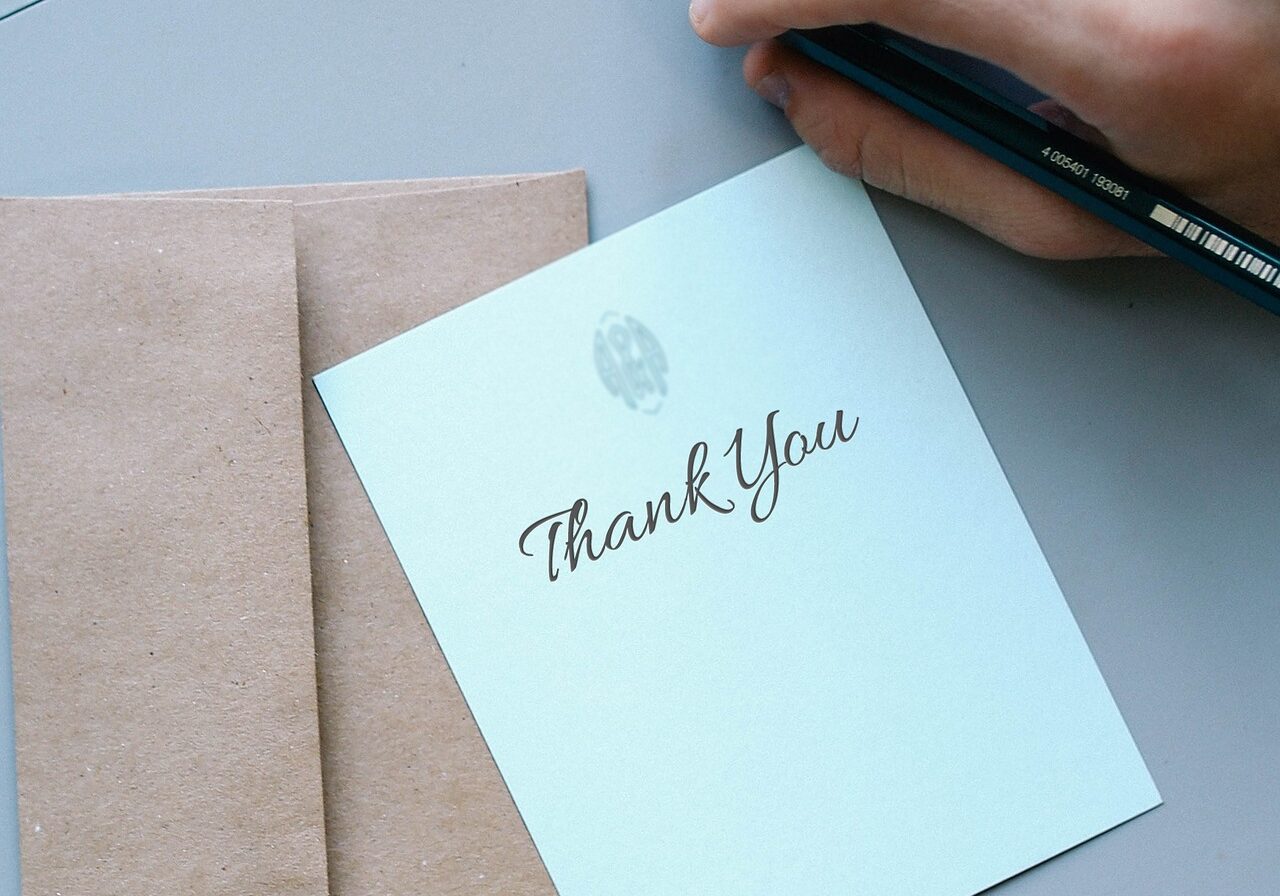 person's hand holding a pencil next to a thank you card and envelope